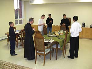 priests and students stand for blessing around table